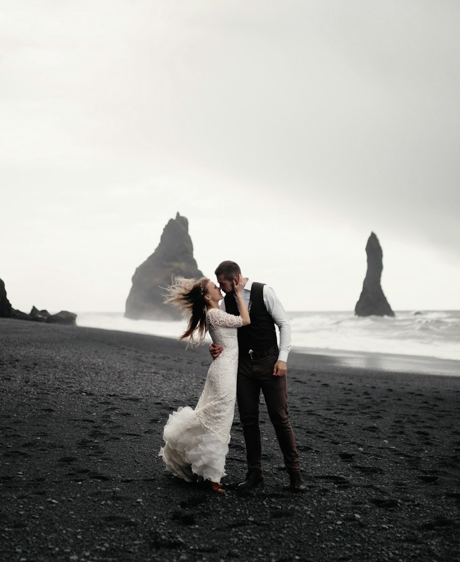 A bride and groom kissing on a windswept beach